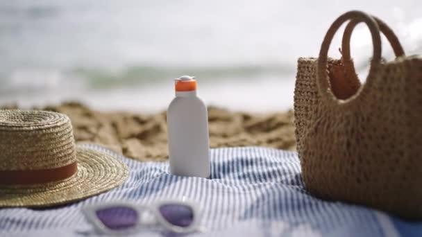 夏のレジャーを体現した編まれたバッグ 晴れたビーチでストライプタオルの日焼け止めボトル 海辺の雰囲気の中で健康な肌のためのエッセンシャル 紫外線から保護 — ストック動画