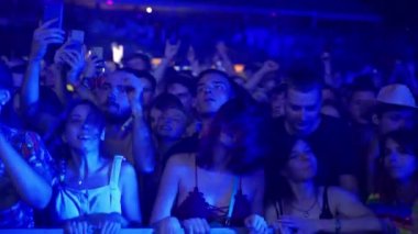 2021-08-08 - Mariupol Şehir Festivali, Ukrayna. Hayranlar dans eder, neon ışıklarda tezahürat yapar, fotoğraf çeker, konser heyecanı yaşar, yazın dışarıda parti havası yaratır. Kalabalık gece festivalinde canlı müzik dinliyor.