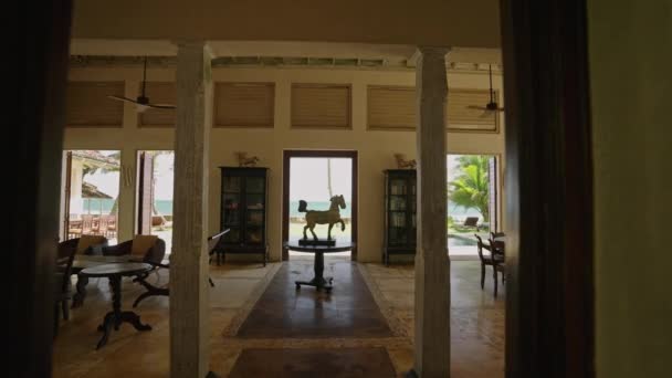 高級レトロヴィラにヴィンテージ家具を備えたリビングルームの中心にある白馬の像 トロピカルアイランドのオーシャンフロントリゾートのヤシの木とプールへのアクセスアートオブジェクト付きの客室 — ストック動画