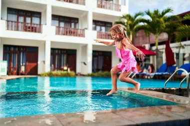 Mutluluk, aktif tatil, su oyunu tasvir edilmiş. Pembe mayolu heyecanlı genç kız güneşli bir tatil köyünde açık havuza atlıyor. Çocukluk, yaz, tatil, seyahat, lüks otel arkaplanı.