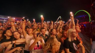 2021-08-08 - Mariupol Şehir Festivali, Ukrayna. Hayranlar telefonlarını ışıklarla sallıyor, canlı performans için dans ediyorlar. Kalabalık müzik festivalinde gece konserinin keyfini çıkarıyor. Açık hava yaz etkinliğinde heyecanlı seyirciler.