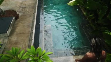 Zarif vuruşlar berrak, sakin, mavi sularda süzülür ve rahatlatıcı tropikal bir kaçış görüntüsü sunar. Üstten drone atışları. Kadın yeşil havuzda huzur içinde yüzüyor..