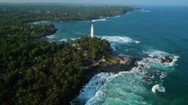 Hava aracı büyük okyanus dalgaları kayalık kıyıları, temiz lagün sularını, tropik körfez manzarasını vuruyor. Yeşilliklerle dolu tropikal adalarda klasik Hollanda deniz feneri stantları.