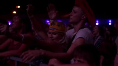 2021-08-06 - Mariupol Şehir Festivali, Ukrayna. Hayranlar kutlama yapıyor, konser veriyor. Müzik festivali kalabalığı gece sahne ışıkları altında dans ediyor. Bir grup genç dışarıda ritim ve neşe hissediyorlar..