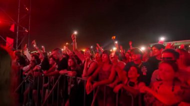 2021-08-08 - Mariupol Şehir Festivali, Ukrayna. Hayranlar el sallıyor, sahne ışıkları altında akıllı telefonlarla kayıt yapıyorlar. Kalabalık canlı müzik seviyor, gece festivalinde dans ediyor. Seyircilerin katılımıyla açık hava etkinlik ortamı.