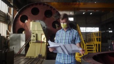 Mekanik uzmanı tasarım ve metal işlerini analiz eder. Koruyucu maske mühendisi sanayi atölyesinin planlarını inceliyor, ağır makineleri, güvenliği ve üretim sürecini geliştirmeyi inceliyor.