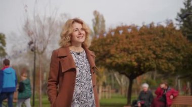 Gülümseyen bayan açık havada sonbahar havasını sever. Sonbahar parkında zarif bir kadın geziniyor, etrafını çevreleyen canlı yapraklar. Keyif yürüyüşü, sakin doğa düzenlemesi. Moda kıyafetleri mevsimlik manzarayı tamamlar.