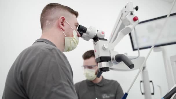 Мужчина Дантист Ассистентом Оперирующего Пациента Зуба Помощью Микроскопа Современной Стоматологической — стоковое видео