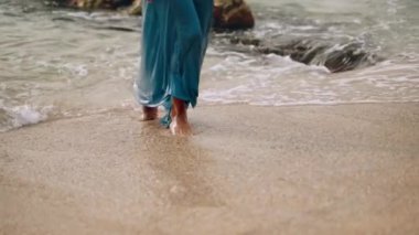 Romantik kaçamak temalar, moda yaşam tarzı, huzurlu bir tatil için mükemmel. Akan elbiseli çıplak ayaklı kadın kumlu plajda denizden çıkar, dalgalar ayaklara vurur, özgürlüğün özü, rahatlama, yaz titreşimleri. Slomo