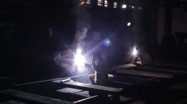 Fabrika zemininde koruyucu maskeli, inşaat alanında metal kaynak yapan endüstriyel kaynakçı, kavis kıvılcımları uçuşuyor, yetenekli tradesperson karanlık atölyede çelik fabrikasında çalışıyor..