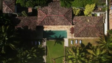 Okyanus yakınlarındaki kumlu tropik bir adada büyük bir retro villanın insansız hava aracı videosu. Bahçesinde yüzme havuzu, verandası ve palmiye ağaçları olan antika lüks yazlık evi manzarası..