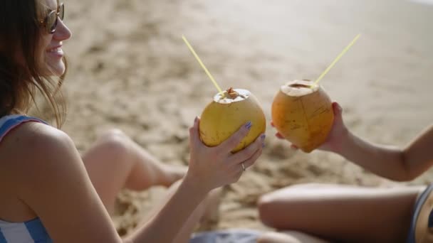 Δύο Χαρούμενα Κορίτσια Μαυρίζουν Ζητωκραυγάζουν Κοκτέιλ Καρύδας Στην Αμμώδη Παραλία — Αρχείο Βίντεο