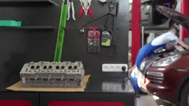 Silindir kafası bankta, alet gereçleri ön tarafta, teknisyenler arkada. Tamirci atölyede motor tamiri yapıyor. Profesyonel hizmet, araç bakımı, tamir süreci belgelendi.