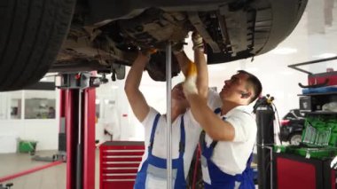 Ekip araba debriyajını kaldırılmış otomobilin altında tamir ediyor, profesyonel servis bakım garajında. Oto tamircileri tamirhanedeki araca şanzıman monte ederek birlikte çalışırlar. Otomotiv teknisyenleri, iş başındaki araçlar.