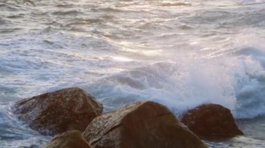 Dalgalar kayalara çarparken altın ışık suya yansıyor. Denizde gün doğumu. Okyanus gücü, doğadaki güzellik ilham verir. Parlayan şafak manzarayı aydınlatıyor, sıcak ortam huzur verici bir izlemeyi davet ediyor. Yavaşla