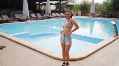 Güzel bir kadın kalıyor, poz veriyor, plaj restoranında yüzme havuzu ve güneşli yaz günlerinde arkadaşlarıyla flört ediyor. Mayolu ve şortlu bir model..