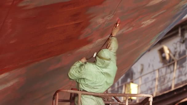 工业涂料 防锈维护 船用船舶整修工艺 防护服工人将红色油漆涂在干船坞的船体上 造船厂工人 使用中的安全设备 — 图库视频影像