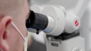 Eczacılık laboratuarında mikroskop kullanarak koruyucu yüz maskesi takan erkek bilim adamının yakın çekimi. Mikrobiyolog aşının mikroskobik testlerini yapıyor. Bilim adamı laboratuarda araştırma örnekleri üzerinde çalışıyor..