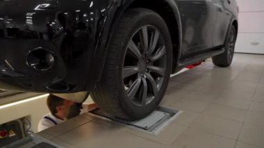 Atölye uzmanı araba güvenliğini, tamir gereksinimleri için tekerlek hareketlerini kontrol ediyor. Otomobil tamircisi modern otomobil servis istasyonunda hidrolik oyun detektörü kullanarak araç süspansiyonunu ve direksiyonunu denetliyor.