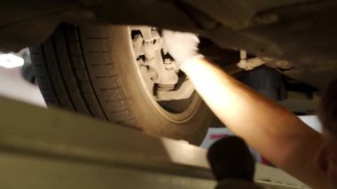 Becerikli teknisyenler bakım ve güvenlik kontrolü için şasiyi inceliyor. Oto tamircisi hidrolik oyun detektörü kullanarak direksiyonu kontrol eder, araba servisinde süspansiyon kullanır. Videoda tamir işlemi.