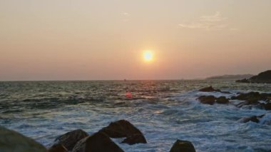 Dalgalar kayalık kıyıya çarpar. Deniz feneri tepede duruyor, gün batımı okyanusun üzerindeki gökyüzünü aydınlatıyor. Doğal güzellik, huzur dolu, dinamik deniz manzarası, akşam karanlığında. Rahatlamak için sakin deniz manzarası, doğa temaları.