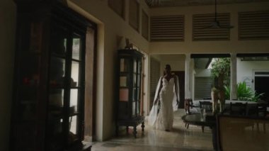 Gey bipoc adam beyaz elbiseli ve şifon peçeli eski moda mobilyalarla lüks bir villada yürüyor. Zenciler düğün fotoğrafı çekimi için Cennet Adası 'ndaki havuza giderler..