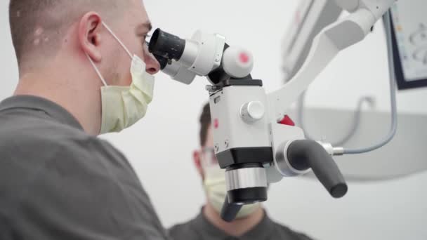 在现代牙科诊所的手术中 应用牙科显微镜对男牙和辅助病人进行了近距离观察 牙科医生 辅助治疗根管 显微镜在牙科中的应用 — 图库视频影像