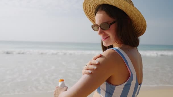 快乐的年轻女子在海滨涂上温泉日光浴 戴草帽的漂亮姑娘把防晒霜涂在皮肤上以防紫外线 穿着比基尼的女士在海上用防晒霜的画像 — 图库视频影像