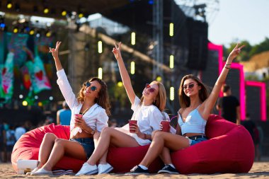 Gündelik yaz kıyafetleri, güneş gözlükleri, canlı festival atmosferi, okyanus manzarası. Gün batımında kırmızı fasulye torbalarında neşeli kızlar, içkilerle tezahürat yapıyorlar, kumsal festivalinde canlı müzik dinliyorlar..