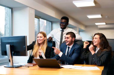 Çeşitli ofis ekipleri bilgisayardaki başarılı anlaşmaya heyecanlı bir şekilde tepki veriyor, büyümeyi kutlayan mutlu çok ırklı meslektaşlar, iş adamı ve iş kadını yumruk tokuşturma kurumsal toplantıda zafer anı paylaşılıyor.