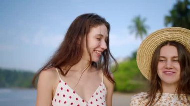 Cennet adasındaki tropikal plajda yürüyen iki mutlu beyaz kız. Neşeli mankenler gider, deniz kenarına gülümser. Genç kaygısız kadınlar okyanus kıyısındaki yaz gezisinde rahatlar, gülerler. Yakın plan..