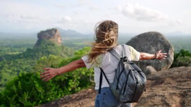 Sigirya Kayası 'nın nefes kesici manzarasının tadını çıkarıyor. Olgun Asyalı kadın kollarını açıp kayalık zirvede özgürlüğü kucaklıyor. Kıdemli yürüyüşçü, doğadaki başarısını, solo seyahat macerasını kutluyor. Yavaş çekim.