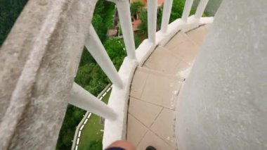 Gezgin dikkatle iniyor, baş dönmelerini yakalıyor yükseklikleri arttırıyor, Sri Lanka 'ya macera yolculuğu yapıyor. POV, Ambuluwawa Kulesi 'nin sarmal merdivenlerinden aşağı inerken, zengin bitkiler yapının etrafını sarar. Yavaşla