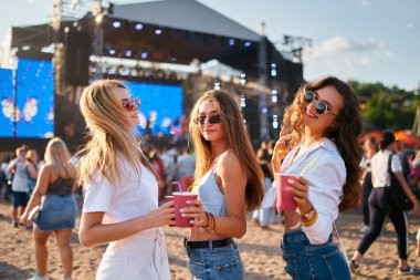 Grup yaz etkinliklerinin, güneşli sahil partilerinin tadını çıkarıyor. Kızlar gülüyor, plaj müzik festivalinde bardaklarla dans ediyor. Güneş gözlüklü genç kadınlar, günlük kıyafetler, eğlenin, içkilerle sosyalleşin..