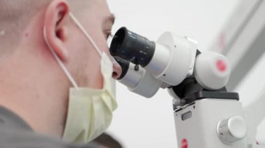 Eczacılık laboratuarında mikroskop kullanarak koruyucu yüz maskesi takan erkek bilim adamının yakın çekimi. Mikrobiyolog aşı testleri yapıyor. Bilim adamı mikroskop kullanarak organik örnekler üzerinde çalışıyor..
