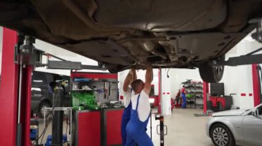 Profesyonel araç altında araç kullanır. Mavi tulumlu oto tamircisi araba debriyajını tamir eder, vites kutusunu atölyeye yerleştirir. Otomotiv servisi, garajda elle şanzıman tamiri. Uzman araba bakımı yapıyor.