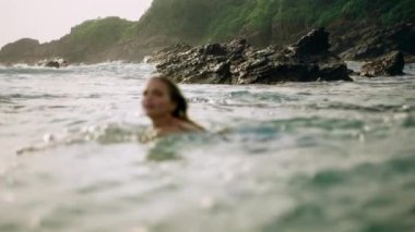 Pürüzsüz giysiler içinde, sakin sudan, rahatlama atmosferinden, altın saatinde doğal sahil manzarasından hoşlanan bir bayan. Zarif kadınlar okyanusta yıkanır, neşeli dalgalar romantik kumsal ortamında ona sarılır. Yavaşla