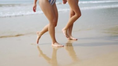 Denizde yıkandıktan sonra sudan çıkan iki dişi arkadaşın ince ayakları. Deniz suyundan çıkıp kumsala giden bikinili neşeli kızlar. Genç güzel kadınlar deniz kenarında eğleniyor. Yavaş çekim.