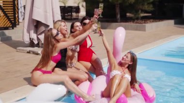 Kadınlar havuzda bikini, bikini ve bardaklarla şampanya içerler. Bayan lüks bir kulüpte şişme flamingo içip kokteyl içiyor. Güneş gözlüklü modeller rahatlar, eğlenirler..