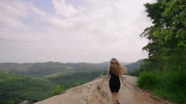 Doğa yolculuğundaki yalnız gezgin, zirvede coşku. Kadın dağa tırmanıyor, zirveye ulaşıyor, kollarını zaferle sonuna kadar açıyor, temiz hava soluyor, geniş tepe manzarası, seyahat, özgürlük, macera. Slomo