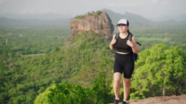 Maceraperest gezgin Sri Lanka manzarasını keşfeder, Asya 'da zengin bitkilerin arasında tek başına yürüyüş deneyimi yaşar. Sırt çantalı aktif kadın yürüyüşçü Sigirya Kayası 'nın yakınından geçiyor. Yavaşla