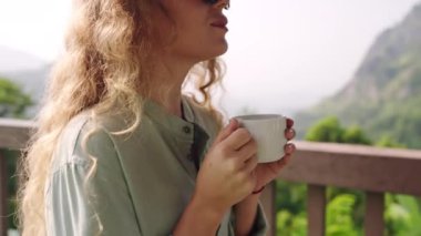 Boş bir sabah, lüks bir tatil evi manzarası. Kadın terasta kahve yudumluyor, dingin dağ zemininde. Solo gezgin güneşin doğuşunu, doğada rahatlamayı sever. Zarif yaşam tarzı, gezgin şehvet anı.
