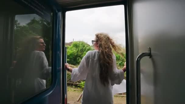 穿着白衬衫的卷发旅行者喜欢旅行 看植物 体验火车旅行的刺激 快乐的女人从火车车厢的窗户向外倾斜 感受着热带美景中的微风 — 图库视频影像
