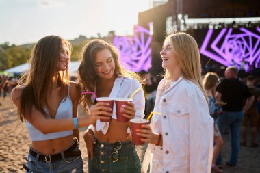 Açık hava parti havası, yaz eğlencesi kalabalık ve festival sahne arkası. Kadınlar plaj müzik festivalinde bardaklarını tokuşturur, mutlu arkadaşlar gün ışığında içkileriyle kadeh kaldırır. Neşeli bir grup kutlama, kahkaha.