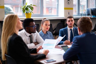 Afrikalı, Asyalı ve beyaz takım üyeleri çizelgeleri tartışıyor, modern ofis ortamında proje üzerinde işbirliği yapıyorlar. Çok ırklı profesyonellerden oluşan bir grup bir iş toplantısına katıldı..