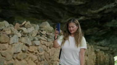 Aktif kıdemli, doğal mağarayı keşfeder, kayalık arazide gezinirken dijital anılar yaratır. Sırt çantalı yaşlı Asyalı kadın dağ patikası kayıtlarına göre akıllı telefondan seyahat ediyor. Yavaş çekim.