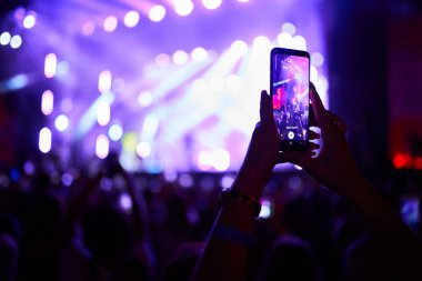Heyecanlı müzik festivali izleyicileri, canlı ışıklar sahneyi aydınlatıyor, hayran kayıtları akıllı telefonda canlı performans, arkadaşlar gece dışarı çıkıyor, orkestra yaz akşamları festival atmosferinde çalıyor.