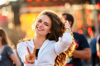 Sıradan kıyafetler, kumda dans etme, neşeli ruh hali, arka planda kalabalığın bulanıklığı, davet edici bir hava için kameraya uzanma. Mutlu genç kadın plajda yaz müzik festivalinin tadını çıkarıyor..