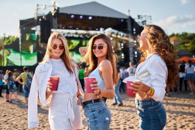 Bir grup mutlu kadın sahilde yaz müziğinin keyfini çıkarıyorlar. Sıradan moda tarzları, eğlenceli atmosferler, soğuk içecekler. Güneşli sahil konserinde üç gülümseyen genç kadın kadehlerini kaldırıyor..