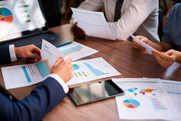 Corporate group collaborates, sharing insights, focusing on data-driven solutions. Multiethnic team analyzes business metrics at workplace, discussing colorful graphs on reports, planning strategy.